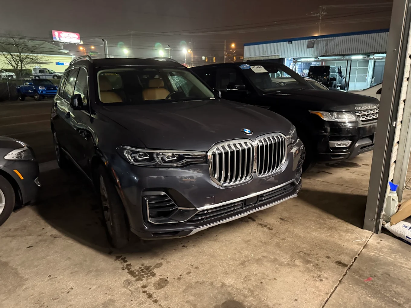 BMW X7 and Land Rover Range Rover parked under the Mentor Auto Service bay awning at night.